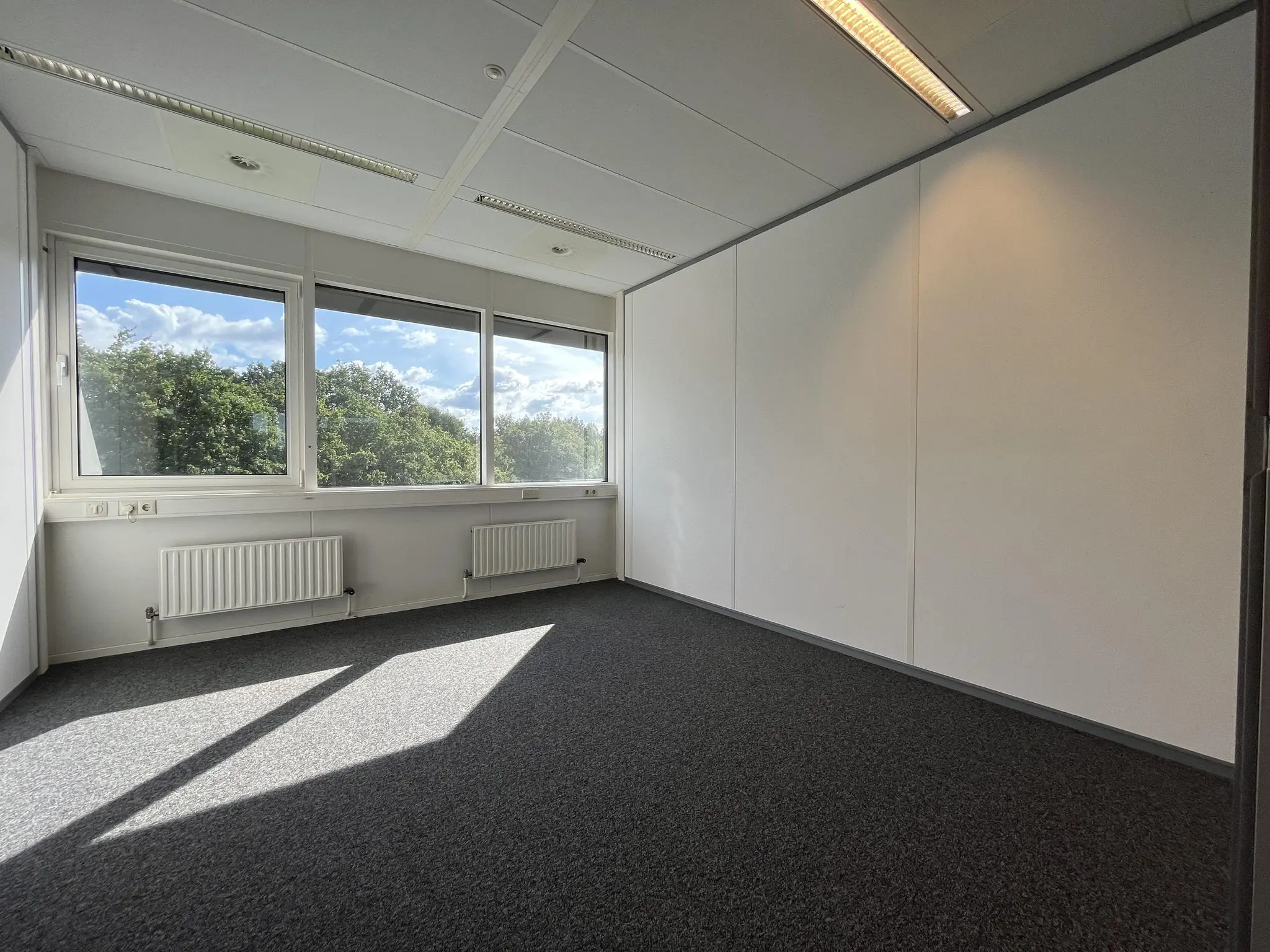 Leeg kantoor met grote ramen en uitzicht op groene bomen aan de Baarnsche Dijk.